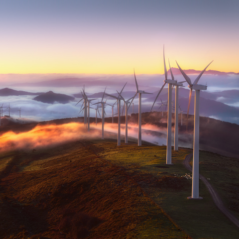 Row of wind turbines on mountaintop with a sunset background